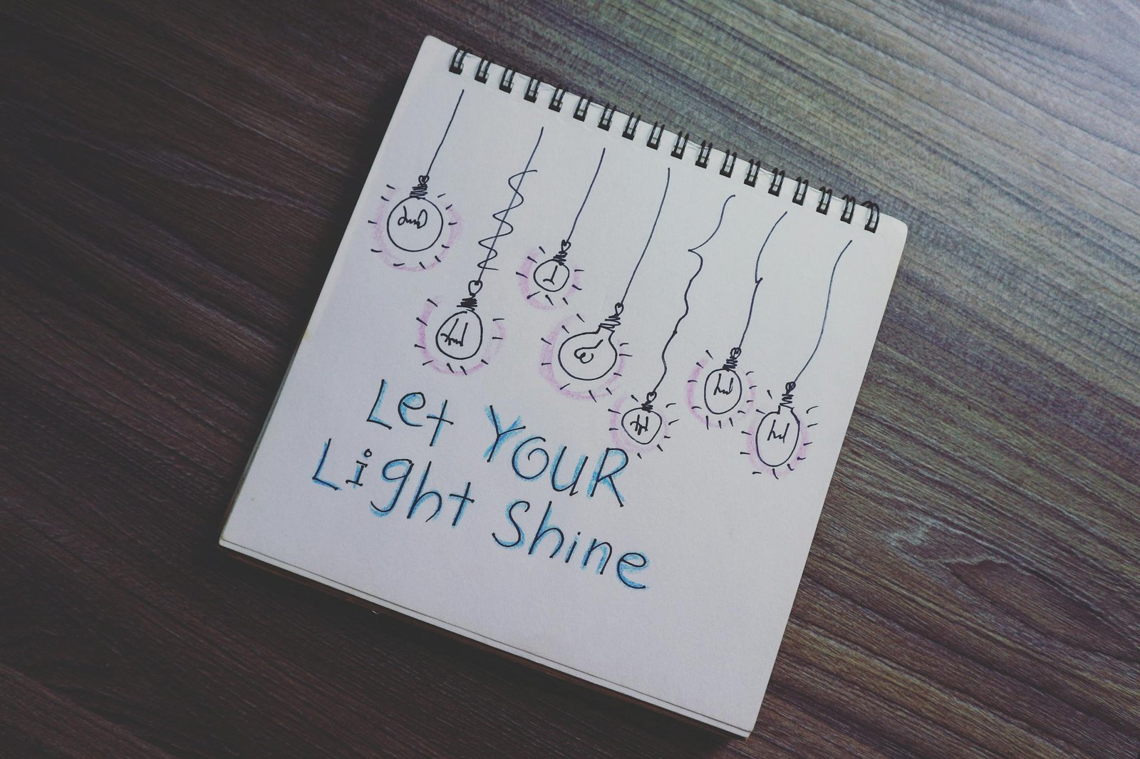 A notebook with a motivational quote and light bulb drawings on a wooden table.